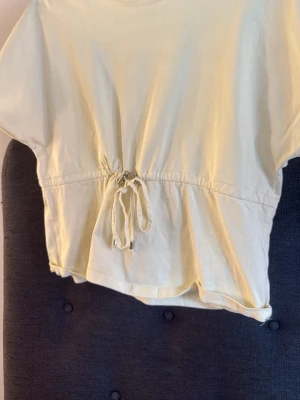 Ljusgul croppad topp med knyt - Snygg ljusgul croppad topp med korta ärmar och knyt i midjan. Toppen har en avslappnad passform och är tillverkad i mjuk bomull, perfekt för en chill och trendig look.