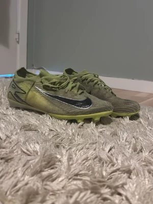 Nike vapor 16 elite  - Säljer ett par gröna Nike fotbollsskor med svart swoosh på sidan och snörning. Skorna har låg profil och är tillverkade i ett lätt syntetmaterial med dobbar för bra grepp på planen. Perfekta för dig som vill ha snabba fötter och snygg stil på matchen.