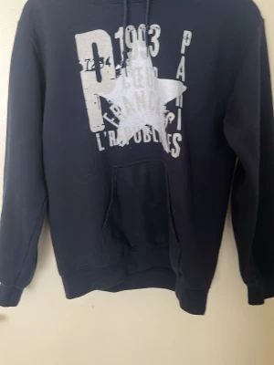 Zandro Studio hoodie - Säljer en svart hoodie med stor vit stjärna och texttryck på framsidan. Hoodien har huva med snöre och en klassisk magficka. Perfekt för en avslappnad streetwear-look.