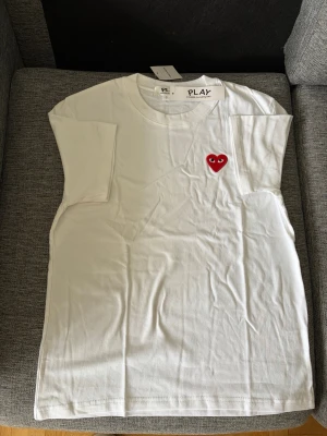 Cdg t shirt - Säljer en klassisk vit t-shirt från Comme des Garçons PLAY med det ikoniska röda hjärtat broderat på bröstet. T-shirten har rund hals och korta ärmar. Perfekt basplagg med en stilren och trendig touch.