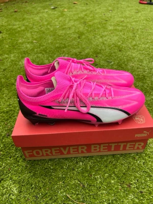 Puma Ultra Ultimate - Puma Ultra Ultimate FG/AG – Strl 44 – Mycket fint skick  Säljer ett par Puma Ultra Ultimate FG/AG i den populära rosa/svarta färgställningen. Skorna är i mycket fint skick och redo att användas direkt.  • Storlek: EU 44 • Modell: Puma Ultra Ultimate FG/AG • Skick: 10/10 (se bilder) • Originalkartong ingår.  Lätta och responsiva fotbollsskor som passar perfekt för dig som vill ha maximal snabbhet och bra bollkänsla. Perfekta för naturgräs och moderna konstgräsplaner.  Skickas snabbt 