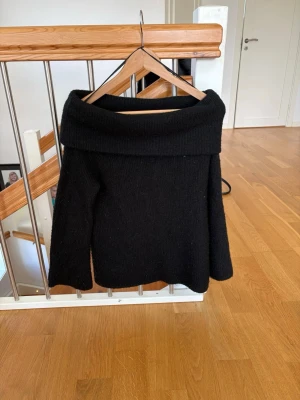 Svart off shoulder stickad tröja H&M - Svart stickad tröja från H&M med bred off shoulder-krage. Tröjan har lång ärm och en avslappnad passform, perfekt för en trendig och mysig look. Materialet är mjukt och bekvämt, passar bra till jeans eller kjol.