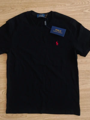 Svart t-shirt från Polo Ralph Lauren - Klassisk svart t-shirt från Polo Ralph Lauren med röd broderad logga på bröstet. Storlek 160-170 cm