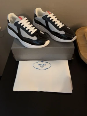 Svarta och vita sneakers - Snygga sneakers i svart och vitt med glansiga detaljer och vita meshpaneler. Skorna har vita snören, tjock vit sula och en modern, sportig siluett. Perfekta för dig som vill ha en clean och exklusiv look.