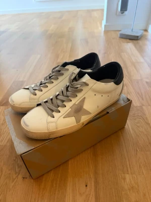 Golden Goose vita sneakers med stjärna - Snygga vita sneakers från Golden Goose med grå stjärna på sidan, använd 2 gånger då dom var för små för mig.