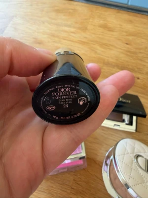 Dior Forever Skin Perfect Stick 2N - Foundationstick från Dior i nyansen 2N. Kompakt och smidig för enkel applicering, perfekt att ha med i väskan. Ger en naturlig finish och är enkel att blenda ut. Förpackningen är svart och elegant med silvriga detaljer.