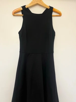 Svart  klänning  - Klassisk svart klänning med rund halsringning och fin design. Klänningen har en enkel, stilren siluett och är tillverkad i ett mjukt tyg som faller snyggt. Perfekt för dig som gillar minimalistisk och tidlös stil. Använd 1 gång 