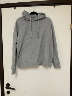 Grå basic hoodie med huva - Enkel och stilren grå hoodie med huva och dragsnören.  Hoodien har avslappnad passform och ribbade muddar vid ärmar och nederkant. Perfekt för en chill och avslappnad look. ( tänk på jag har hund i hemmet) 