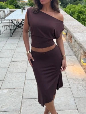 Brun offshoulder topp - Trendig brun offshoulder topp med lös passform och kort ärm. Toppen har en asymmetrisk skärning som ger en cool och avslappnad look. Perfekt att matcha med kjol eller jeans för en snygg outfit.