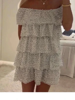Vit prickig volangklänning offshoulder - Supersöt vit kortklänning med svarta prickar och flera volanglager. Offshoulder-modell som ger en trendig och somrig vibe. 