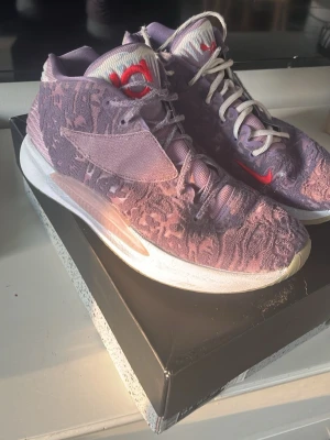 Kd shoes  - Unika lila Nike Air Jordan sneakers med texturerad ovandel i tyg och röda detaljer på tungan och sidan. Skorna har vita snören och en tjock vit sula med genomskinliga partier. Perfekta för dig som vill sticka ut med din sneakerstil.