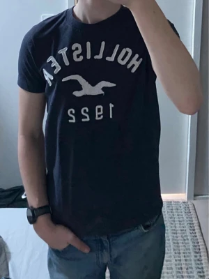 Mörkblå Hollister t-shirt - Snygg mörkblå t-shirt från Hollister med vit logga och texten '1922' framtill. Klassisk passform och rund halsringning. Perfekt till jeans för en avslappnad look.