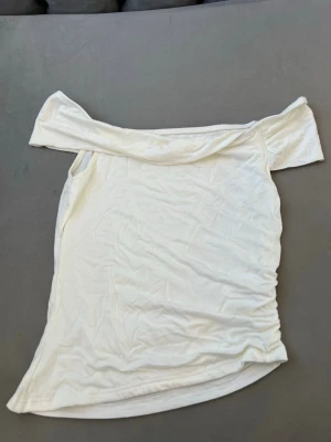 Vit offshoulder topp - Snygg vit offshoulder topp med korta ärmar. Toppens material känns mjukt och stretchigt, perfekt för en trendig och avslappnad look. Passformen är figurnära och toppen har en enkel, stilren design.