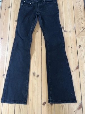 Svarta bootcut jeans - Säljer ett par svarta bootcut jeans med knappar ibak. Jeansen har normal midja och är tillverkade i ett mjukt denimtyg. Är i helt perfekt pasform om man vill ha fler vilder så är det bara att säga till