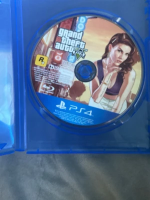 Grand Theft Auto V till PS4 - GTA V till Playstation 4, ett actionfyllt open world-spel från Rockstar Games. Omslaget har en färgstark illustration med neonljus och en kvinna i fokus. Skivan är blå och passar till PS4-konsol.