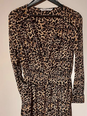 Snygg Zara leopardklänning med skinn-detaljer stl M 🐆🖤 - Säljer denna supersnygga långärmade leopardklänning från Zara Basic i storlek M. Den har omlott-ringning, en stretchig resår i midjan runt om som ger en jättefin form, och sjukt snygga dolda detaljer i svart läderimitation runt ärmarna samt fina detaljer på axlarna. Sitter otroligt fint på och känns väldigt lyxig! Mått platt mätt: * Byst: ca 44cm * Midja: ca 30cm(stretchig resår) * Axelbredd: ca 39cm * Armlängd: ca 57cm * Längd: ca 84–85cm Ansvarar inte för postens slarv🫶