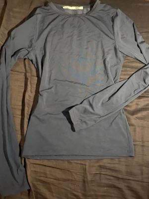 Mörkblå långärmad topp - En enkel och stilren mörkblå långärmad topp med rund hals. Toppen har en slim passform och är tillverkad i ett mjukt och stretchigt material som känns skönt mot huden. Perfekt att matcha med jeans eller kjol för en clean look.