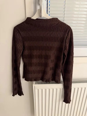 Brun långärmad topp med struktur - Snygg brun långärmad topp med unik strukturerad yta och lätt croppad passform. Perfekt att styla med jeans eller kjol för en trendig look. Materialet känns mjukt och följsamt mot kroppen.
