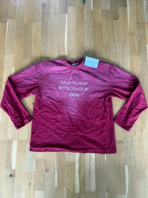 Vinröd sweatshirt Acne Studios - Vinröd sweatshirt från Acne Studios med tryck 'Acne Studios STOCKHOLM 1996' på bröstet. Tröjan har rund halsringning och långa ärmar. Tillverkad i mjuk bomull för en avslappnad look. Perfekt för dig som gillar streetwear och skandinavisk design.