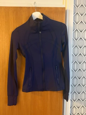 Blå Define Jacket från Lululemon - Snygg blå Define Jacket från Lululemon i mjukt och stretchigt Nulu-material. Jackan har figurnära passform, hög krage, tumhål och två dragkedjeförsedda fickor. Perfekt för träning eller som ett sportigt lager till vardags.