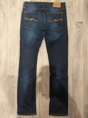 Nudie Jeans Mörkblå W29/L32 - Slim Fit - Nudie Tube Kelly mörkblå jeans med slim fit passform som sitter snyggt och bekvämt och funkar till allt, storlek W29/L32, midja 38,5 cm, ytterbenslängd 102,5 cm, benöppning 17 cm, modellen är 185cm & väger 65kg, i fint skick.