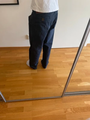 Mörkblå baggy jeans från YSL - Säljer ett par mörkblå baggy jeans från Yves Saint Laurent med avslappnad passform och raka ben. Jeansen har klassiska fem fickor och en liten YSL-logga på bakfickan. Perfekta för en chill och street-inspirerad stil.