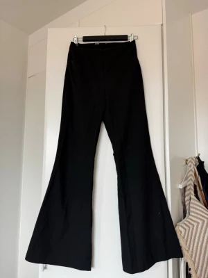 Svarta utsvängda jeans - Säljer ett par svarta jeans med hög midja och utsvängda ben. Snygg passform som ger en retrovibe och passar perfekt till sneakers eller boots. Materialet känns mjukt och stretchigt för extra komfort. Perfekta för dig som gillar trendiga siluetter.