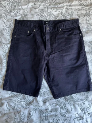 H&M mörkblå shorts – Regular Fit, strl 33 - Stilrena mörkblå shorts från H&M i modellen Regular Fit. Klassisk 5-ficksmodell som passar perfekt till sommaren, semestern eller vardagsbruk. En lättmatchad bas i garderoben som fungerar lika bra med t-shirt som skjorta.