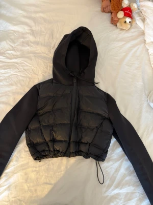 Svart cropped pufferjacka med huva - Säljer en svart cropped pufferjacka med huva och dragkedja framtill. Dragsko i nederkant för justerbar passform. Från Zara storlek S pris kan diskuteras