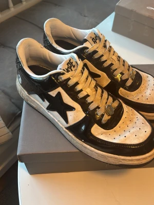 Svarta och vita BAPE STA sneakers - Säljer ett par BAPE STA sneakers i svart och vitt med klassisk stjärndesign på sidan. Skorna har låga skaft, perforerad tå och glansiga svarta detaljer i läder samt vita partier i matt. Går säkert att tvätta av och få fina igen! Inga skador. 