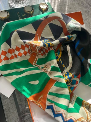 Färgstark mönstrad  sjal - Säljer en lyxig  sjal i siden med färgstarkt mönster i grönt, svart, orange, vitt och inslag av blått och gult. Sjalen har detaljer som hästmotiv, rutor och grafiska former. Perfekt accessoar för att lyfta din outfit.
