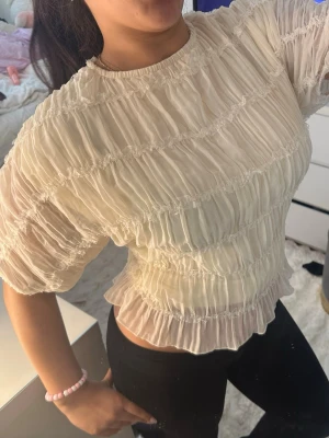 Vit volangblus med kort ärm - Säljer en söt vit blus med volangdetaljer och korta ärmar. Blusen har ett plisserat tyg som ger en luftig och romantisk känsla. Perfekt för dig som gillar en feminin och trendig stil.