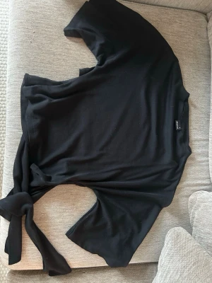 Svart knytblus från Gina Tricot - Säljer en svart blus från Gina Tricot med korta ärmar och snygg knytning i ryggen. Oanvänd 