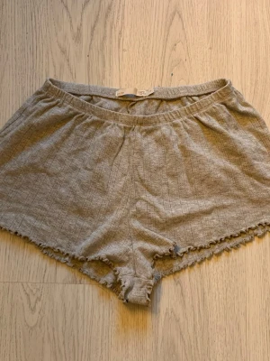 Grå pyjamasshorts från 157 - Mysiga grå pyjamasshorts från 157 i storlek XS. Shortsen har en mjuk resår i midjan, diskreta vertikala ränder och söt volangkant nedtill. Perfekta för chillkvällar hemma. 