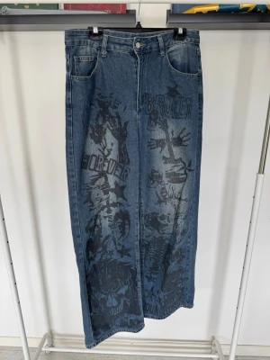 Blåa jeans med tryck - Säljer blåa jeans med straight passform och coolt svart tryck framtill med text och grafiska detaljer. 