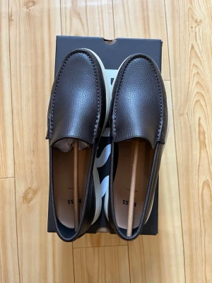 Bruna loafers i läder från BOSS - Stilrena bruna loafers från BOSS i äkta läder med diskret struktur. Skorna har en klassisk form, ljus sula och minimalistisk design som passar till många outfits. Perfekta för dig som gillar en clean och tidlös look.