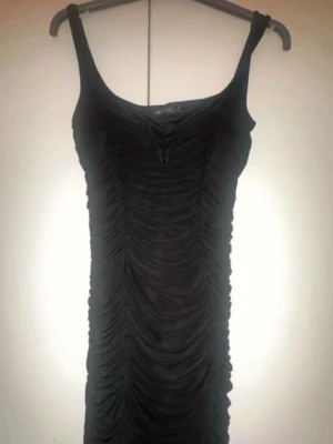 Svart tight klänning från NLY One - Snygg svart tight klänning från NLY One med rynkade detaljer framtill. Klänningen är ärmlös med smala axelband och har en kroppsnära passform som framhäver figuren. Perfekt för dig som vill ha en stilren och trendig look.