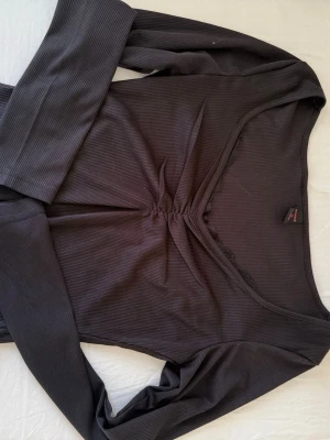 Svart ribbad långärmad topp - Säljer en svart ribbad långärmad topp med v-ringning och snygg rynkdetalj framtill. Toppen har diskret spetskant längs urringningen för en extra touch. Perfekt att styla med jeans eller kjol.