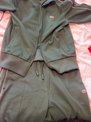Grön Lacoste dress - Säljer min Lacoste dress. Koftan har en dragkedja och byxorna är raka i S storlek. Haft på mig dem 1 gång, inte min stil längre tyvärr. Jättefin skick och perfekt för dig som vill ha den