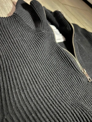 Svart ribbstickad tröja med dragkedja från Jack and Jones! - Säljer en svart ribbstickad tröja med halv dragkedja framtill och hög krage. Tröjan har lång ärm och är tillverkad i ett tjockare stickat material som ger en cool och stilren look. Perfekt för lager på lager och enkel att matcha. Fråga på!