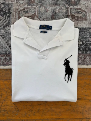 Vit pikétröja Big Pony från Polo Ralph Lauren - Hej! 👋 Säljer en riktigt fräsch vit Polo Ralph Lauren "Big Pony" pikétröja i storlek L. Har den stora broderade svarta loggan på bröstet och siffran ”3” på höger ärm. 🐎✨ Tröjan är i mycket fint skick och välvårdad. Det finns en jätteliten prick på magen, men den syns bara vid extremt noga inspektion och är praktiskt taget osynlig vid användning. 100% äkta med originaltvättlappar (ingen QR-kod på denna modell). Perfekt sommarfräscht premium-basplagg! Fraktar snabbt! 🚛📦💬 