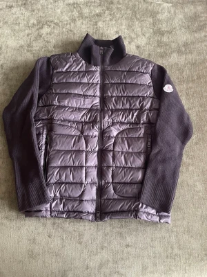 cardiganjacka från Moncler - Snygg lila cardiganjacka från Moncler med quiltad framsida och stickade ärmar och rygg. Jackan har dragkedja framtill, ståkrage och två fickor med dragkedja. Moncler-logga på ena ärmen. Perfekt för lager-på-lager-stil.