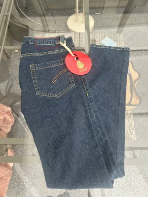 Dondup Jeans – Mod. Joy – Stl 42 / W28 (Helt nya!) - Säljer ett par helt nya jeans från italienska Dondup, modell "Joy". De kommer fortfarande med original-tags kvar. Dondup är känt för sin höga kvalitet och fina hantverk. Modellen Joy har en snygg mörkblå tvätt med snygga kontrasterande sömmar. Tack vare 2% elastan i materialet får du en skön passform med lagom stretch. Kort info:  Märke: Dondup  Modell: Joy  Storlek: 42 (Italiensk storlek, motsvarar ca W28)  Material: 98% bomull, 2% elastan  Skick: Helt nya med tags 