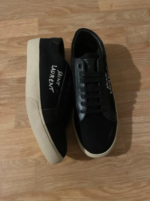 Saint laurent skor svarta  - Säljer ett par stilrena svarta Saint Laurent sneakers. Klassisk och tidlös modell som passar till både vardag och mer uppklädda outfits. Skorna är i fint skick med normala tecken på användning. Bekväma och exklusiva med den ikoniska Saint Laurent-loggan på sidan.  Kvitto finns vid köp. Boxen finns tyvärr inte kvar.