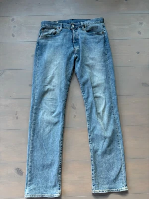 Blå raka jeans från Levi's - Säljer ett par klassiska blå jeans från Levi's med rak passform och fem fickor. Jeansen har en ljus tvätt och är tillverkade i bomull. Perfekta för en avslappnad och stilren look.