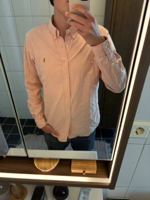 Ljusrosa skjorta från Polo Ralph Lauren - Säljer en ljusrosa skjorta från Polo Ralph Lauren i slim fit. Skjortan har klassisk krage, knappar framtill och den ikoniska broderade loggan på bröstet. Tillverkad i mjuk bomull och har långa ärmar med knapp vid manschetten.