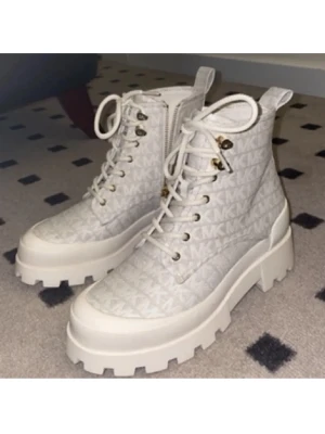 Chunky vita boots från Michael Kors - Säljer ett par chunky vita boots från Michael Kors med grov sula och snörning. Skorna har MK-logga över hela ovandelen, dragkedja på sidan och detaljer i guld. Tillverkade i syntetmaterial och textil, perfekta för en trendig look✨storlek US7
