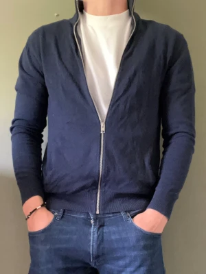Mörkblå ziptröja - Mörkblå ziptröja från Jack & Jones med ståkrage och hel dragkedja framtill. Tröjan har ribbade muddar vid ärmslut och nederkant, samt en smal passform.