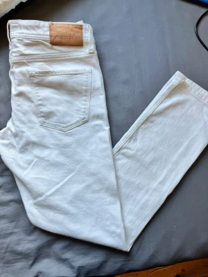Vita jeans  - Säljer ett par vita jeans med klassisk femficksmodell och raka ben. Jeansen har en snygg läderpatch bak i midjan och är tillverkade i ett mjukt bomullsmaterial. Perfekta för dig som vill ha en clean och fräsch look.
