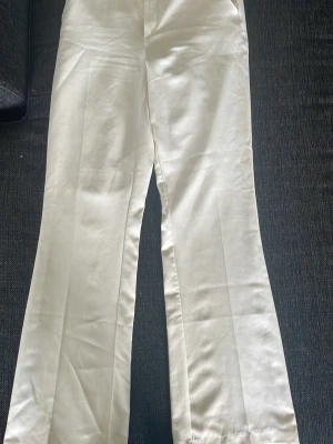 Vita raka kostymbyxor - Snygga vita kostymbyxor med rak passform och pressveck. Byxorna har hög midja och är tillverkade i ett lätt och luftigt linnematerial, perfekta för en stilren och fräsch look. Passar till många olika outfits och ger en clean vibe.